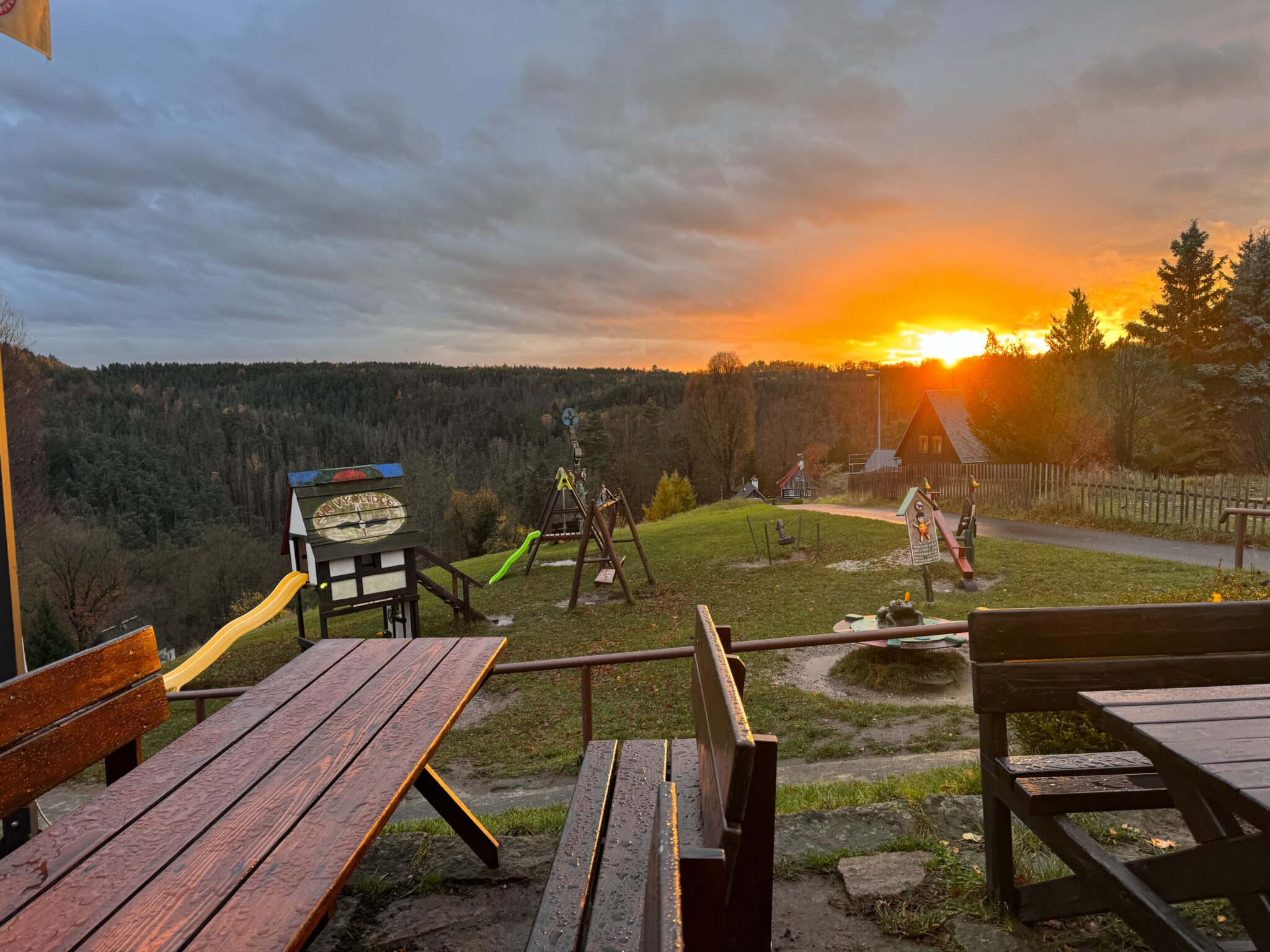 Terasa restaurace Resort Mezná s výhledem na západ slunce, dřevěné lavice, dětské hřiště a krásná přírodní scenérie Českého Švýcarska.